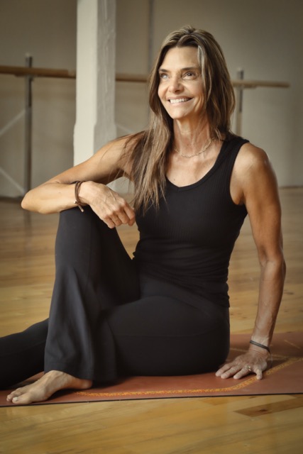 Photo of Chrissy Pike King sitting in a yoga studio with one knee up and her arm resting on her knee.